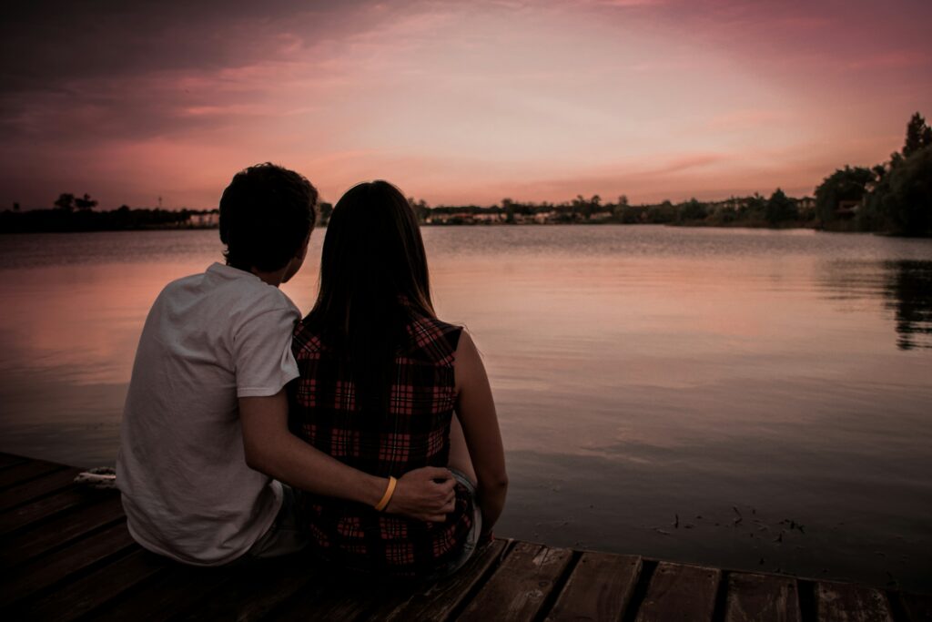 a man and woman sitting on a dock looking at the water